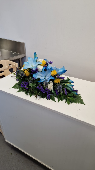 Blue Remembrance - A striking funeral spray in blue, purple, yellow and white tones, designed as a meaningful final tribute.