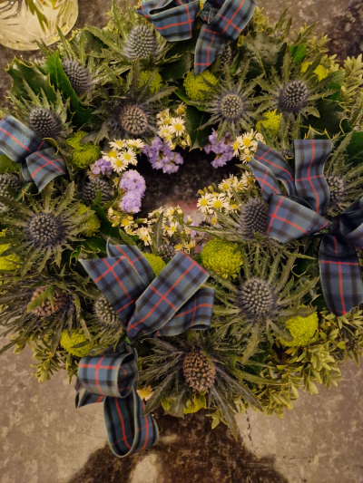 Highland Memories - A distinctive funeral wreath with rich greenery, purple tones and tartan detailing for a traditional feel.